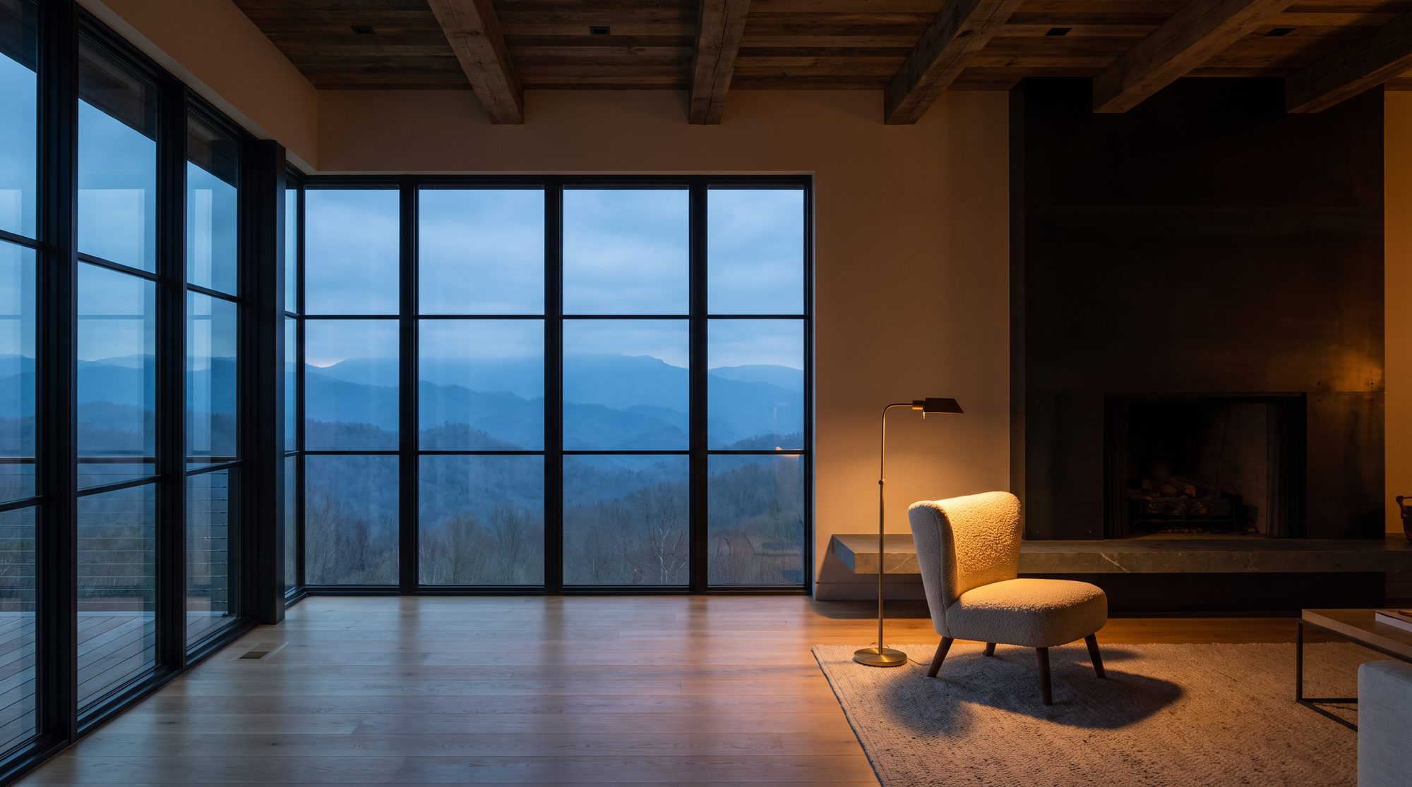 A dark timber-framed living room with floor-to-ceiling steel glazing looking out over layered Smoky Mountain ridgelines